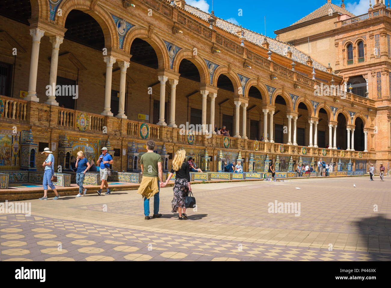 Voyage en Espagne, vue d'un jeune couple de touristes marchant devant une grande colonnade sur la Plaza de Espana un après-midi d'été, Séville, Andalousie, Espagne. Banque D'Images