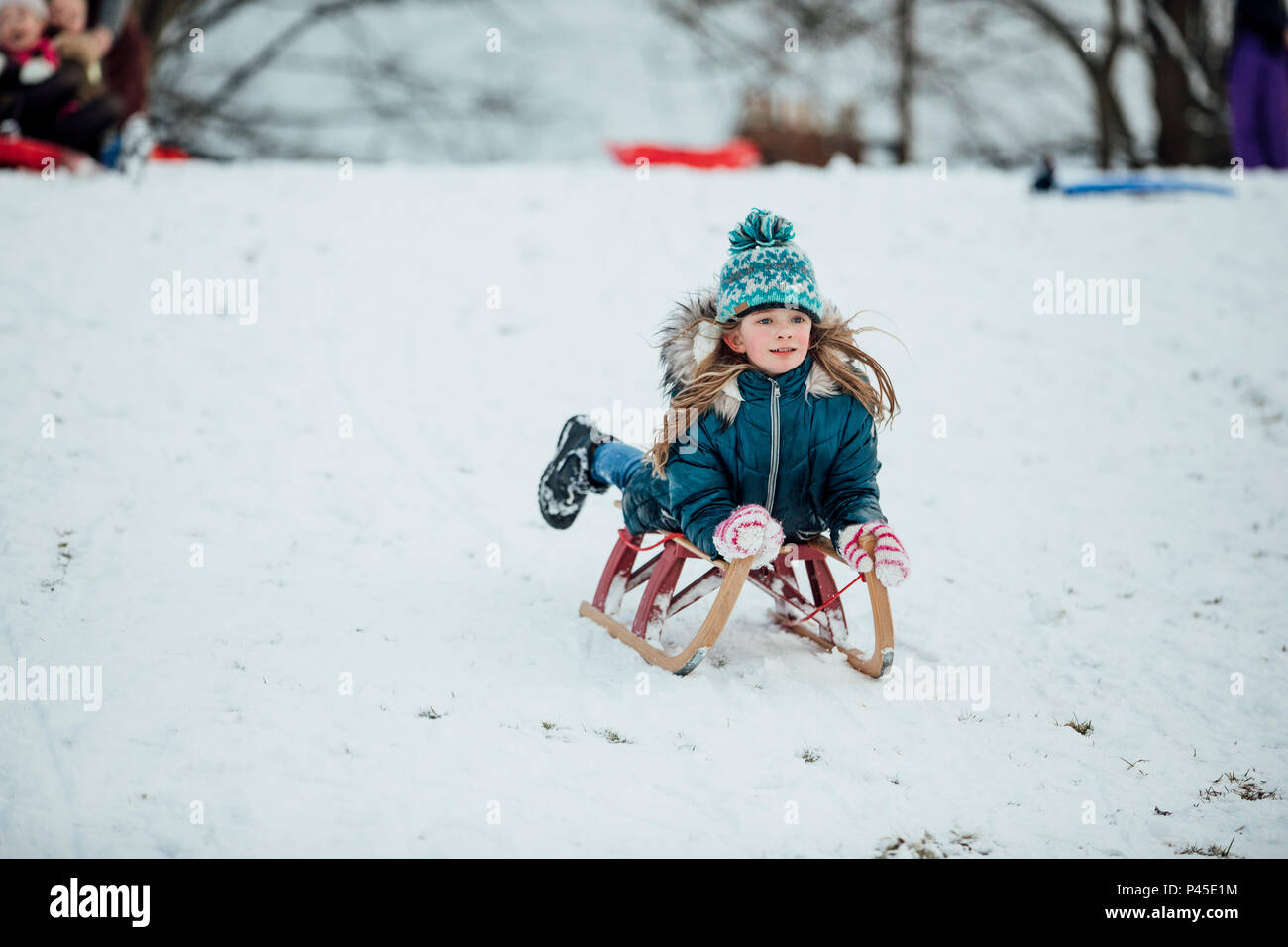 Petite fille est couchée sur un traîneau sur son ventre, descendant une colline de neige dans un parc public. Banque D'Images