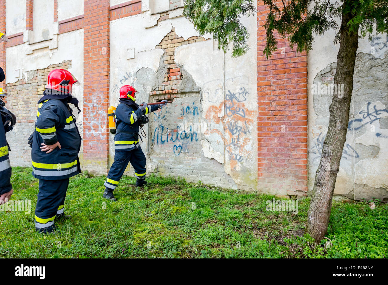 Vue de derrière le pompier en uniforme avec un équipement de sécurité, à l'aide de pince pour briser un mur de briques. Banque D'Images