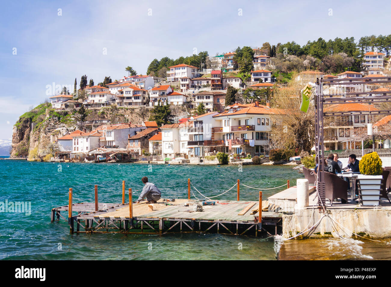 Ohrid, République de Macédoine : Les gens s'asseoir à l'extérieur d'un restaurant par une jetée sur le lac d'Ohrid avec une vue générale de la vieille ville classée Unesco en b Banque D'Images