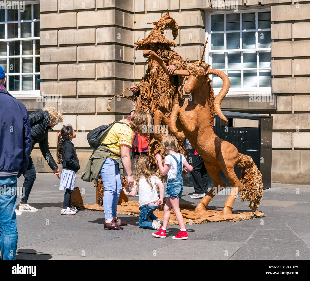 Edinburgh, Ecosse, Royaume-Uni, 21 juin 2018. Un artiste de rue dans une loi de lévitation habillé comme Gandalf l'assistant avec une licorne pour divertir les passants par sur le Royal Mile pendant la saison estivale. Une femme et des enfants sont divertis par la loi sur la rue que les gens passer Banque D'Images