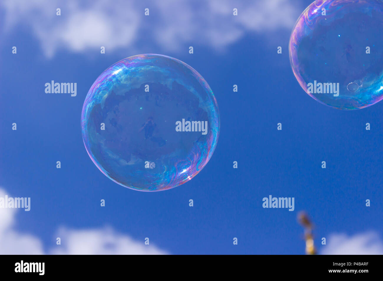 Une bulle de savon irisée flotte dans un superbe ciel bleu. Un coup d'œil à la bulle révèle le reflet du photographe et de City Plaza. Banque D'Images
