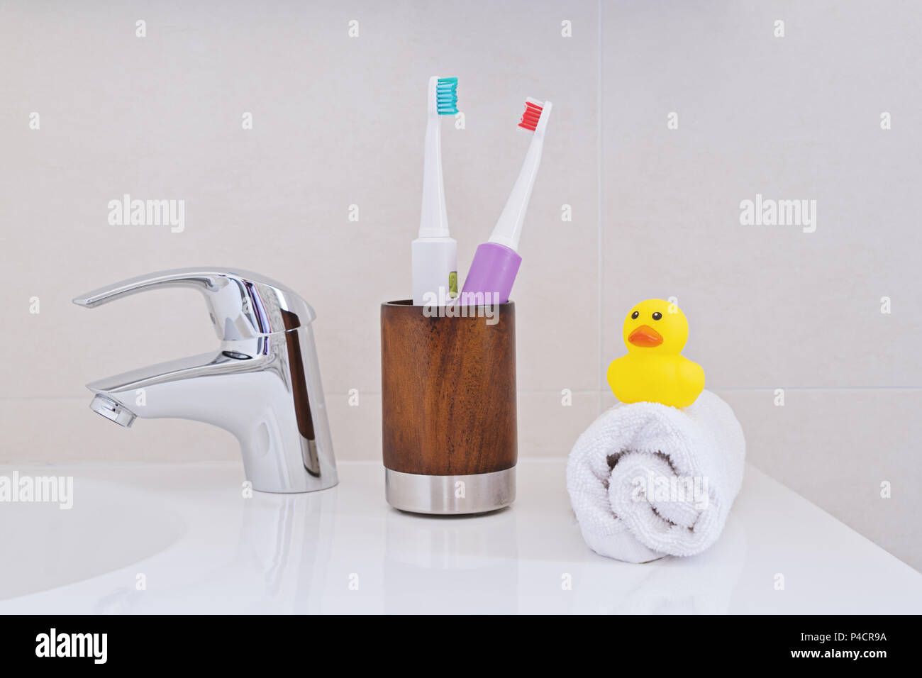 Deux brosses à dents en bois verre sur l'évier dans la salle de bain avec une serviette enroulée blanc et jaune canard ducky en caoutchouc. Concept d'hygiène personnelle. Banque D'Images