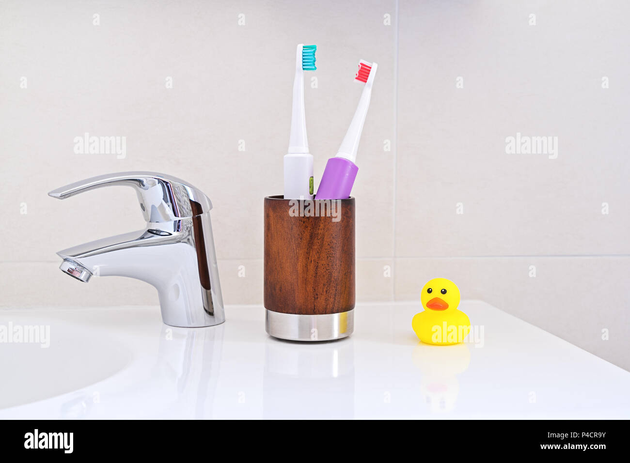 Deux brosses à dents en bois verre sur l'évier dans la salle de bain en caoutchouc jaune ducky duck. Concept d'hygiène personnelle. Banque D'Images