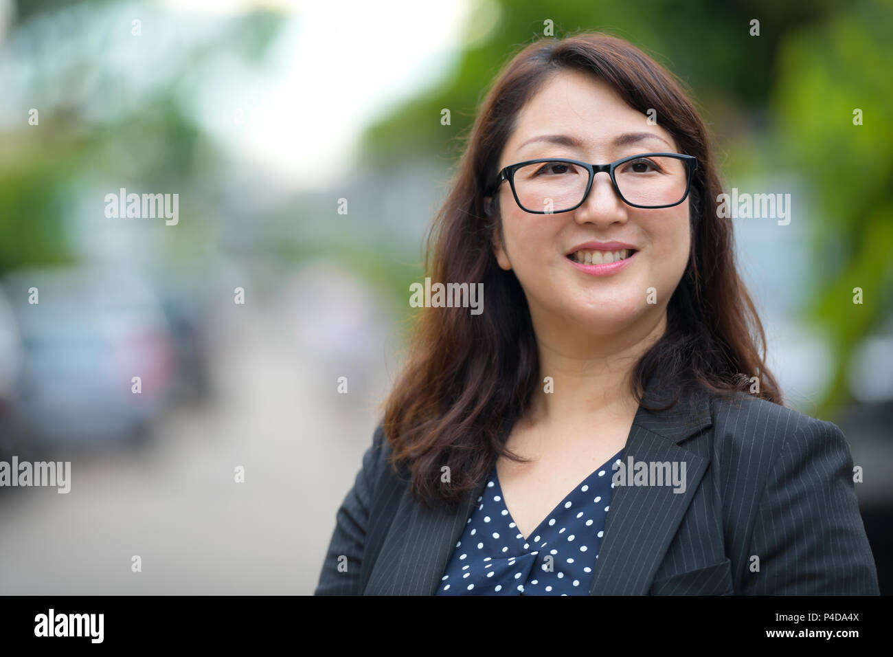 Happy mature Asian businesswoman smiling et penser dans les rues à l'extérieur Banque D'Images