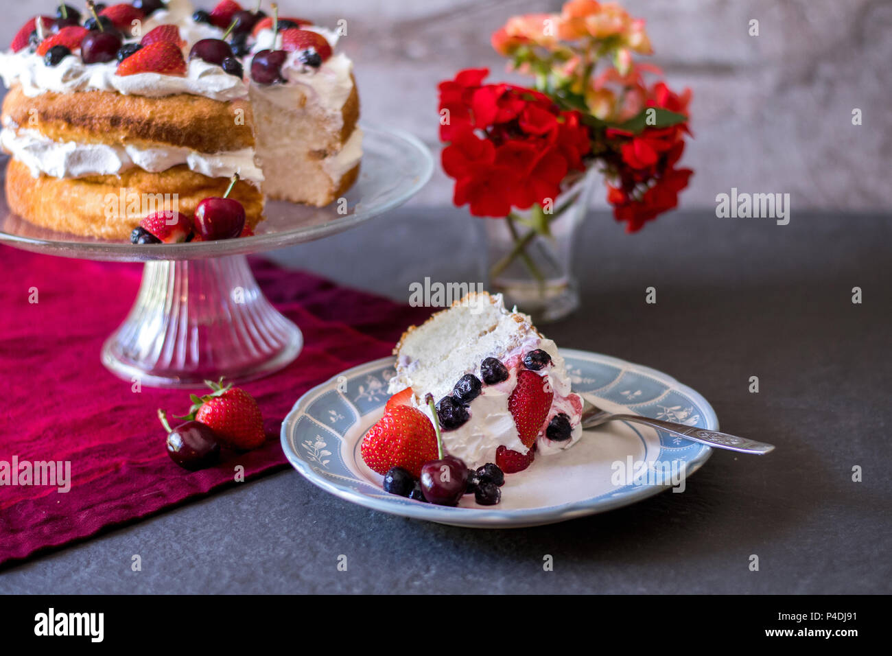 Une belle tranche de gâteau angelfood couvert de crème fouettée et de fruits frais, coloré avec des fleurs et des fruits Banque D'Images