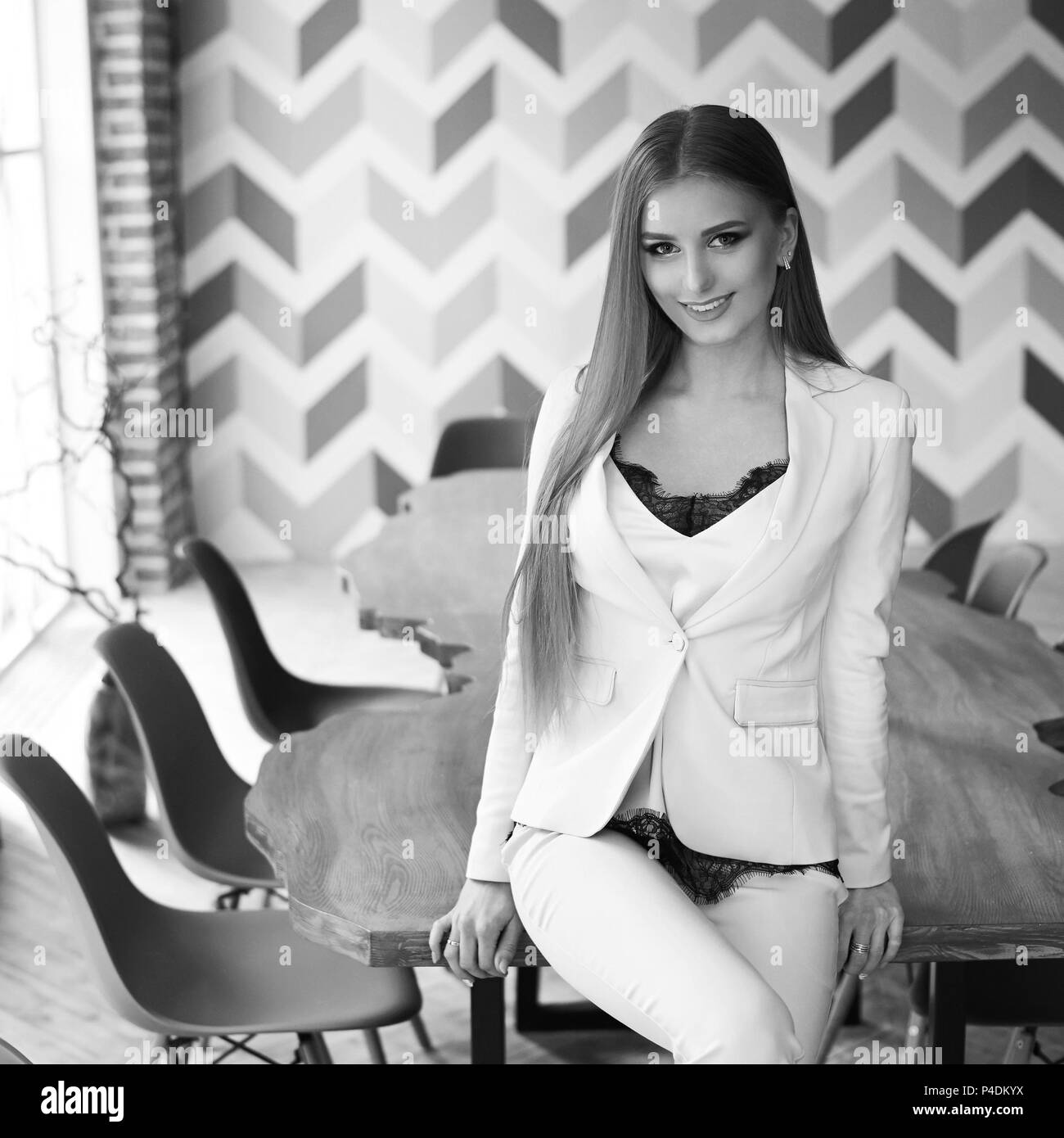 Belle jeune femme aux longs cheveux blonds tout droit en costume bleu assis à table en bois dans l'élégant intérieur moderne. La foudre naturelle Banque D'Images