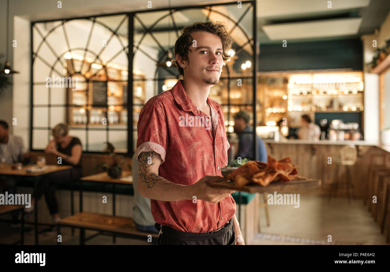 Jeune serveur tenant une assiette de nachos fraîchement cuits au four Banque D'Images