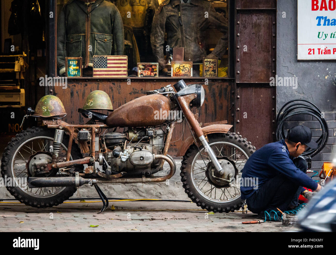 Hanoi, Vietnam - Mars 15, 2018 : l'homme assis en face d'une boutique de style militaire plein de symboles de guerre vietnamiens Banque D'Images