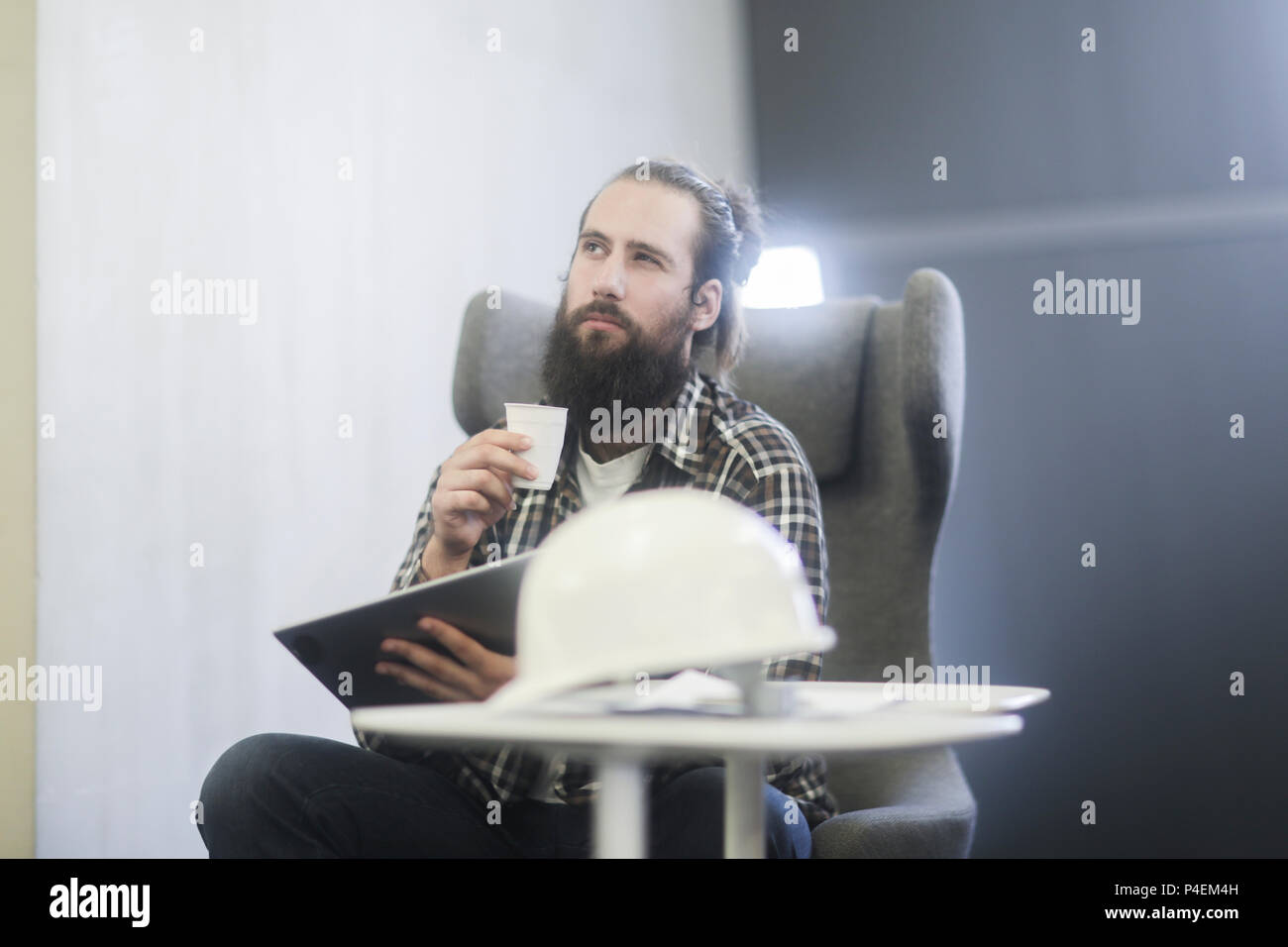 Homme assis dans un fauteuil à l'aide d'une tablette numérique avec un casque de sécurité sur la table Banque D'Images