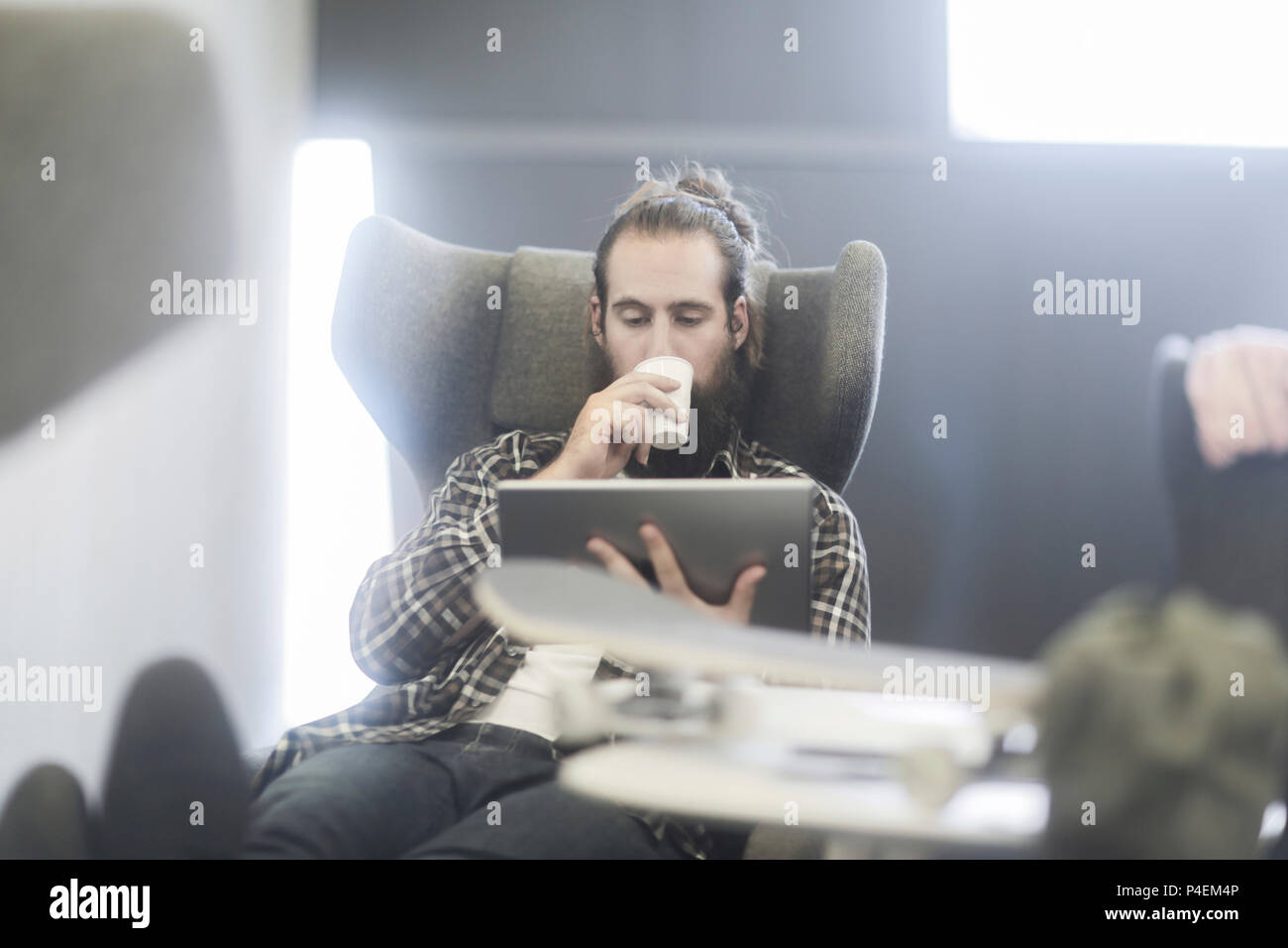 Homme assis dans un fauteuil à l'aide d'une tablette numérique avec une planche à roulettes sur la table Banque D'Images