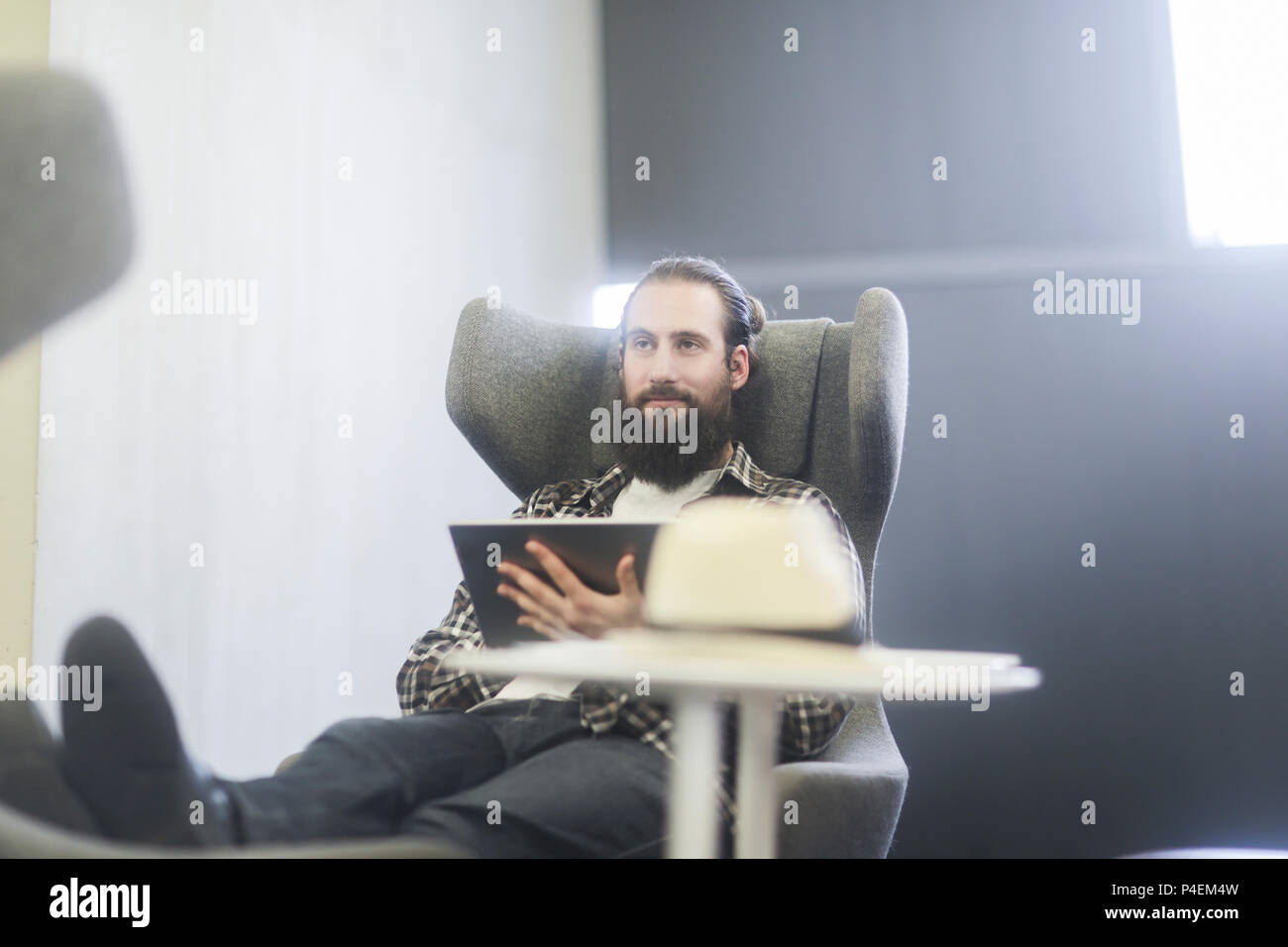 Homme assis dans un fauteuil à l'aide d'une tablette numérique Banque D'Images