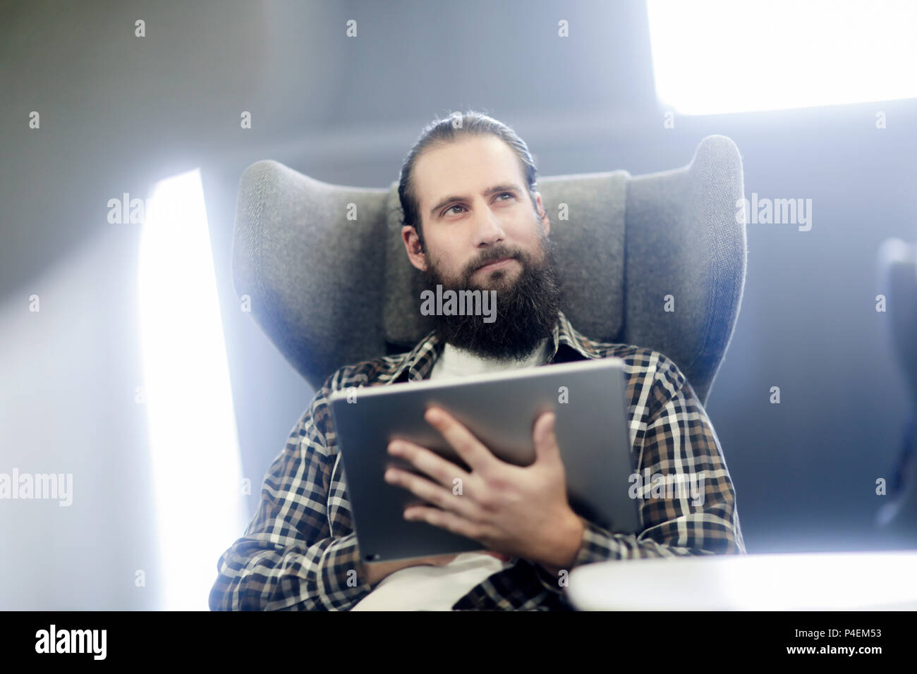 Homme assis dans un fauteuil à l'aide d'une tablette numérique Banque D'Images