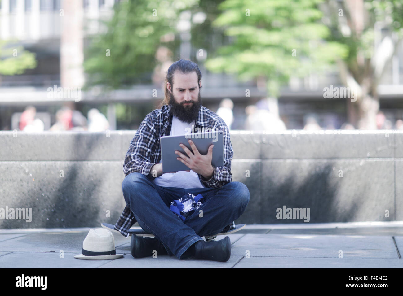 Homme assis sur sa planche à roulettes à l'aide d'une tablette numérique Banque D'Images