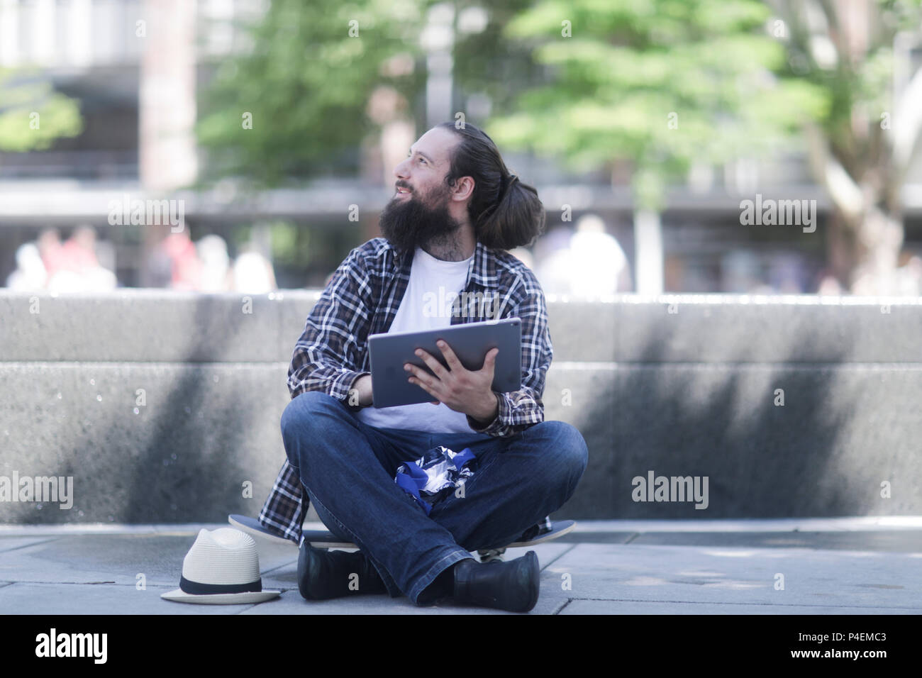 Homme assis sur sa planche à roulettes à l'aide d'une tablette numérique Banque D'Images