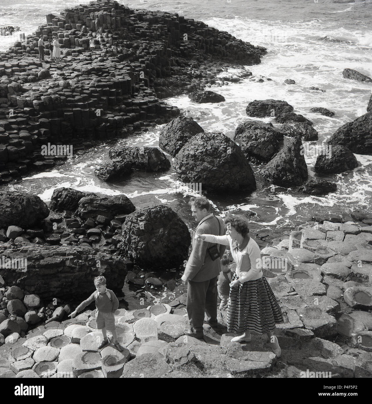 Années 1950, historique, la mère, le père et leur jeune garçon sur le rock hexagonal à colonnes le célèbre Giant's Causeway, le comté d'Antrim, en Irlande du Nord. Cette zone côtière unique de colonnes de basalte, le résultat d'une ancienne fissure volcanique éruption est une merveille de la nature. Banque D'Images