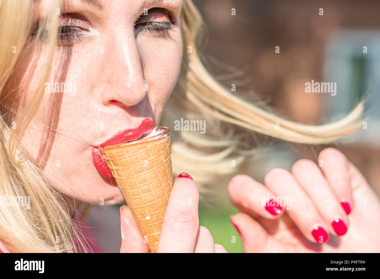 Young attractive woman eating ice cream on chaude journée d'été.Les gens authentiques Uk.Vrai monde.enchanté et ferme les yeux.cheveux blonds en agitant le vent. Banque D'Images