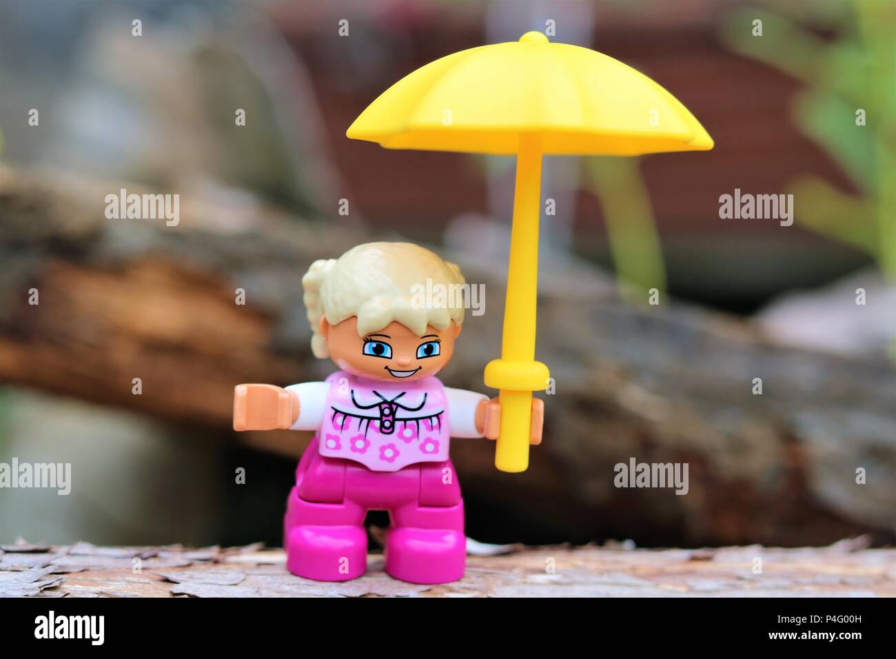 Duplo girl holding a caractère parapluie jaune contre un arrière-plan flou - News Concept Banque D'Images
