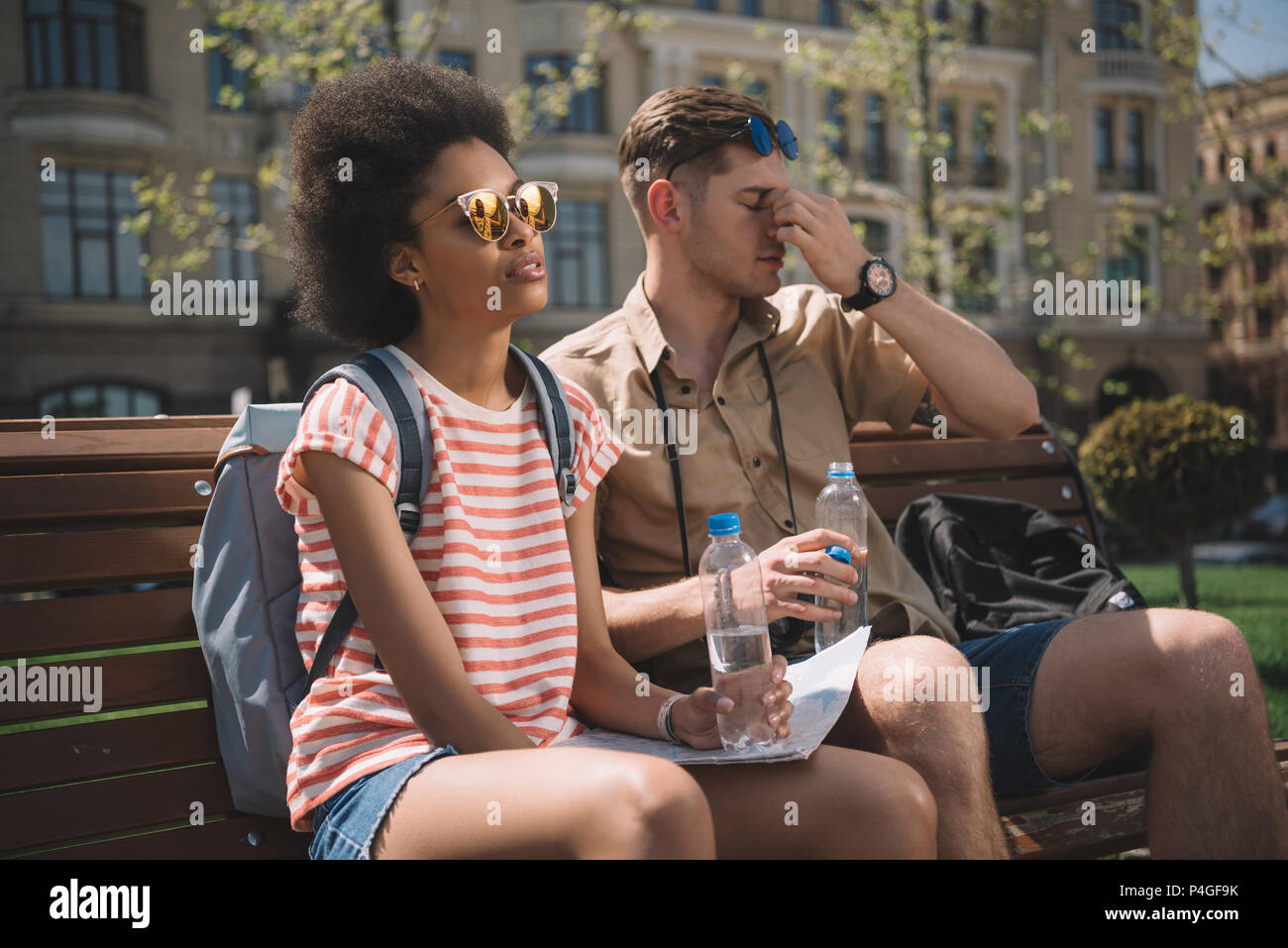 Fatigué couple interracial de voyageurs avec des bouteilles d'eau et plan assis sur un banc Banque D'Images