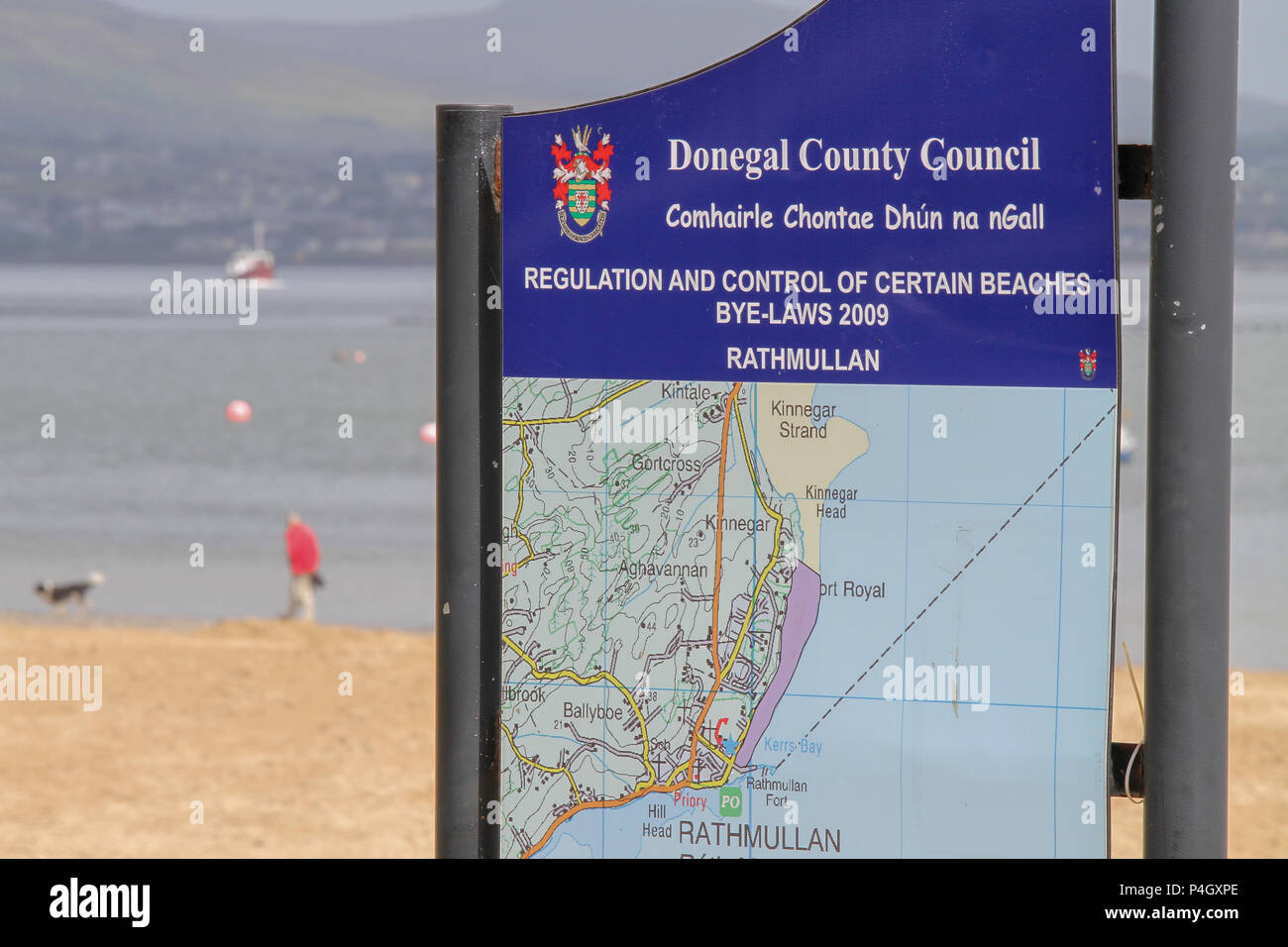 Man Walking dog sur la plage derrière l'Irlande Donegal County Council et de l'information texte d'application signe à Rathmullan beach Lough Swilly, comté de Donegal Irlande Banque D'Images