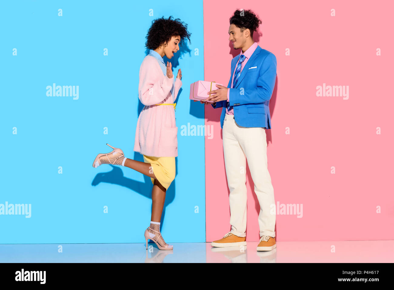 Young African American man boîte cadeau fille donne sur fond bleu et rose Banque D'Images