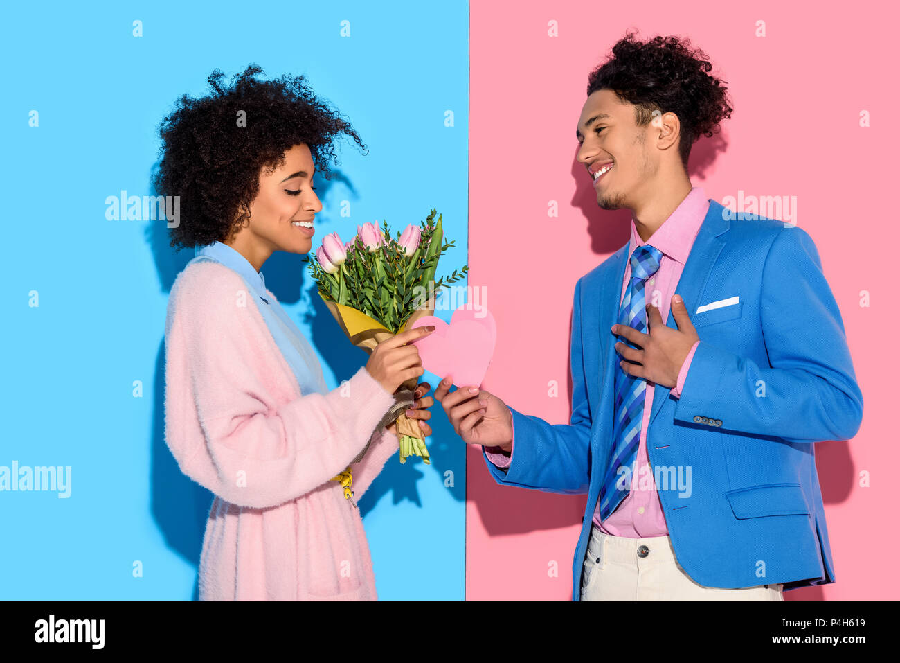 Young African American man girl offre un bouquet de fleurs et coeur carte sur fond bleu et rose Banque D'Images