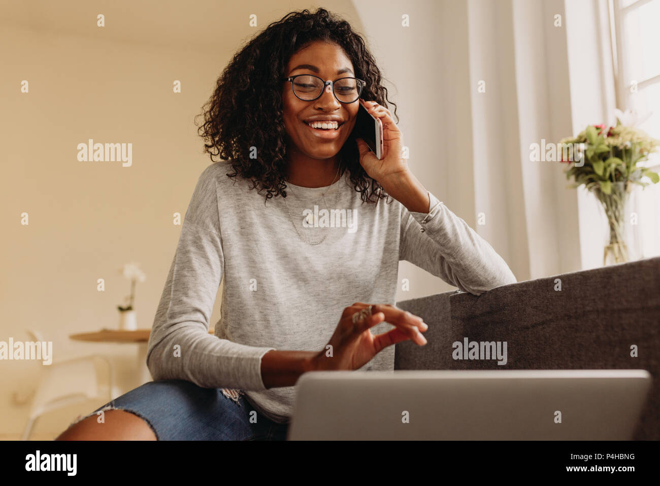 Businesswoman sitting on sofa at home et de conversations au téléphone mobile tout en travaillant sur l'ordinateur portable. Femme à la mode en jean déchiré working on laptop Banque D'Images