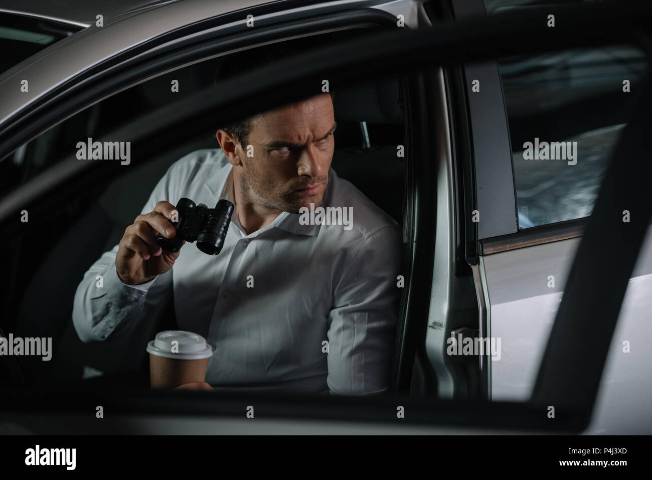 Undercover agent concentré de sexe masculin faisant de la surveillance exercée par des jumelles et de boire du café en ca Banque D'Images