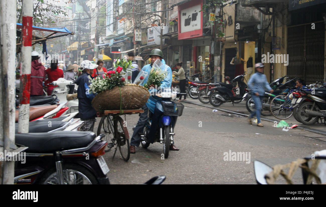 Dame vietnamienne Vente de fleurs de son vélo dans la rue animée de Hanoi, Vietnam Banque D'Images