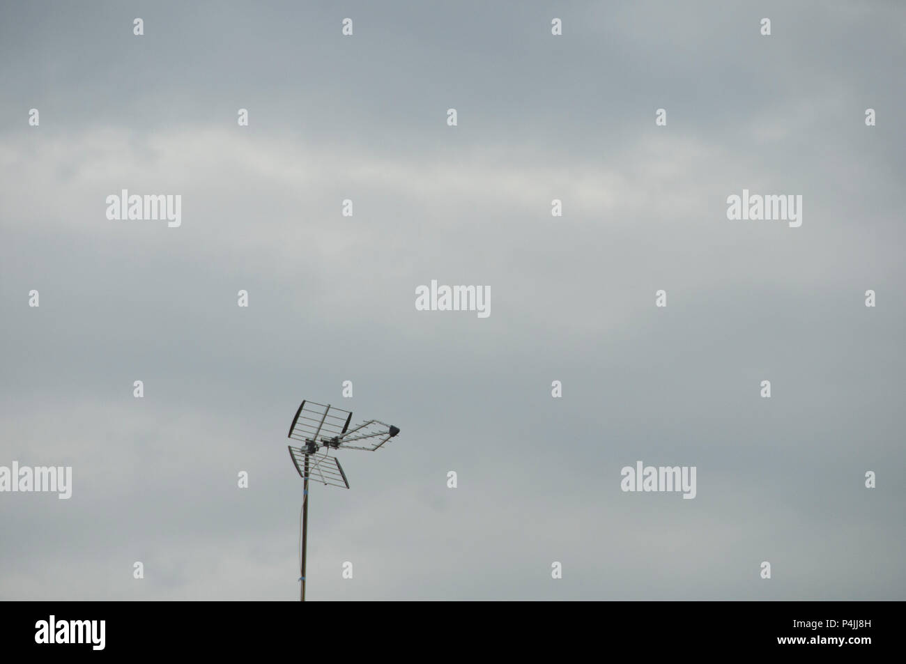 Old style TV par antenne / l'antenne sur le dessus de toit de tuiles noires contre ciel nuageux. Banque D'Images