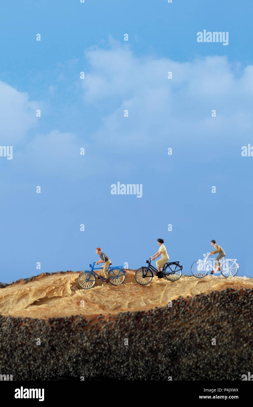 Les gens miniature : un groupe de cyclistes profitez de rouler sur une route de campagne, avec un ciel bleu sur l'arrière-plan Banque D'Images