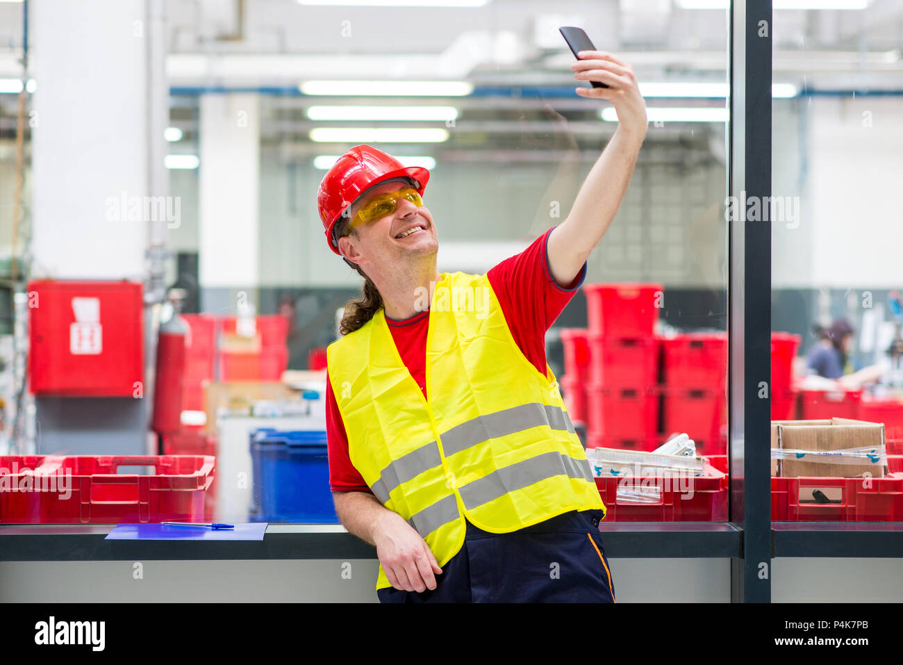 Travailleur dans l'ouest réfléchissant avec casque rouge en tenant dans une usine selfies Banque D'Images