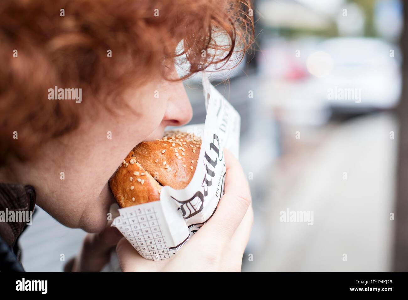 Un adolescent aux cheveux roux mordre dans un hamburger Banque D'Images