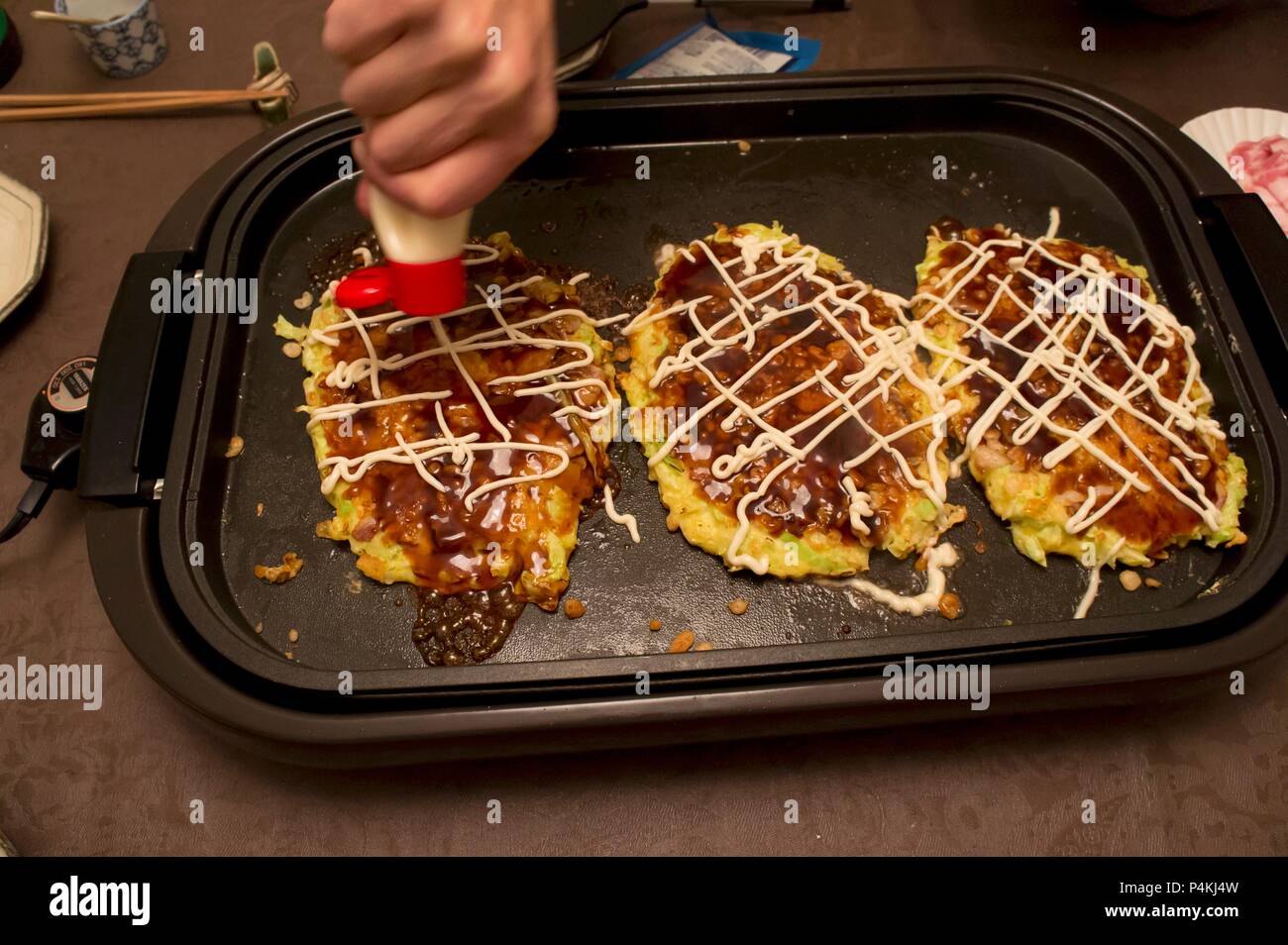 Crêpes okonomiyaki (japonais) sur un plateau chaud sont décorées avec de la mayonnaise Banque D'Images