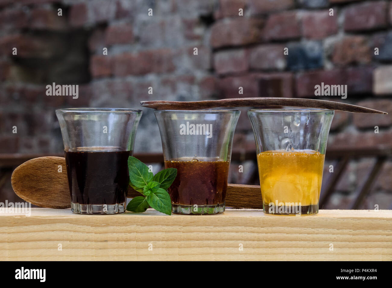 Trois différents types de miel dans des verres disposés en une rangée o un morceau de bois. Décorées avec des cuillères en bois et une feuille de menthe. Banque D'Images