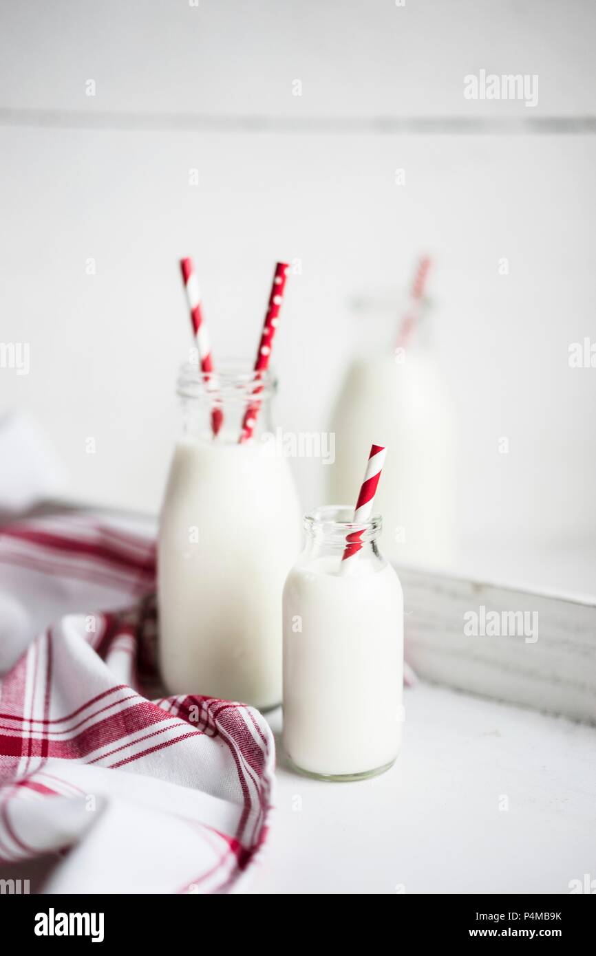 Bouteilles de lait avec du rouge et blanc pailles à rayures sur une surface en bois blanc Banque D'Images