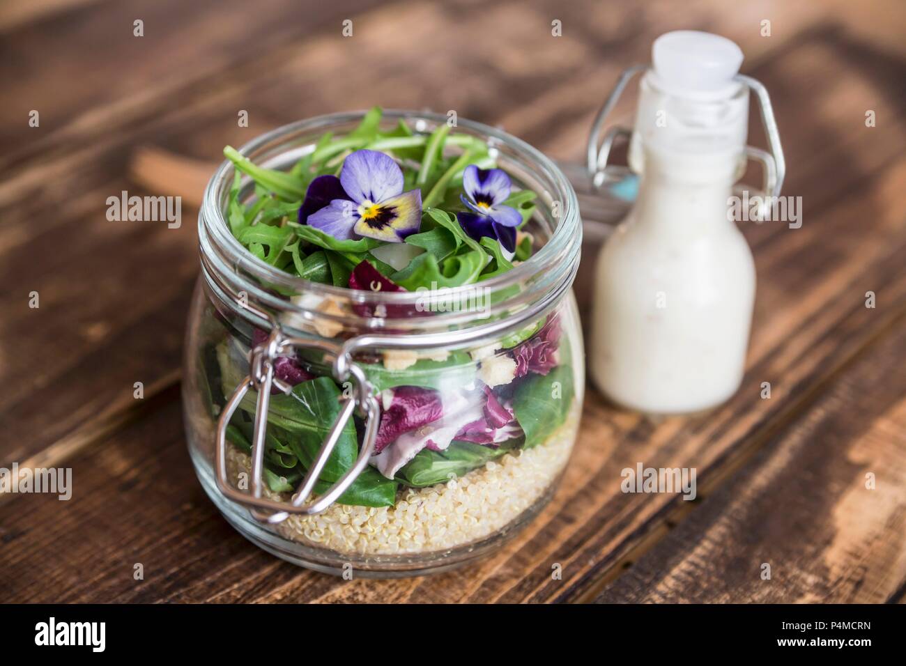 Une Salade de quinoa aux agneaux avec laitue, chicorée, roquette, croûtons, fromage de chèvre et violettes cornu dans un bocal en verre, avec la vinaigrette dans une bouteille en verre Banque D'Images