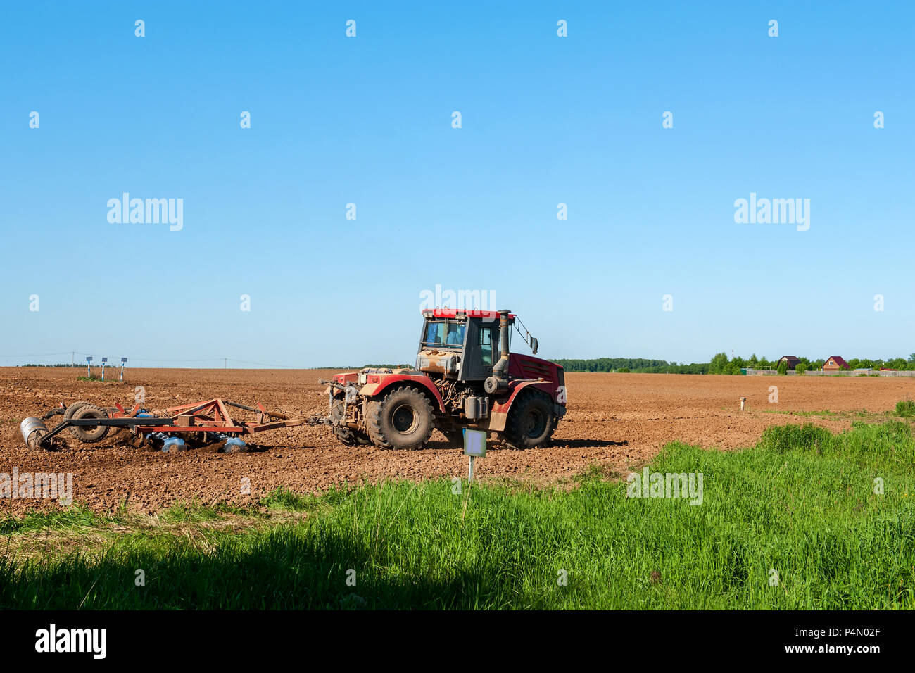 Grand format argent tracteur avec un rotoculteur à disques herse rouge sur le terrain sur une journée ensoleillée. Le concept de travail dans un champs et industrie de l'agriculture. Banque D'Images
