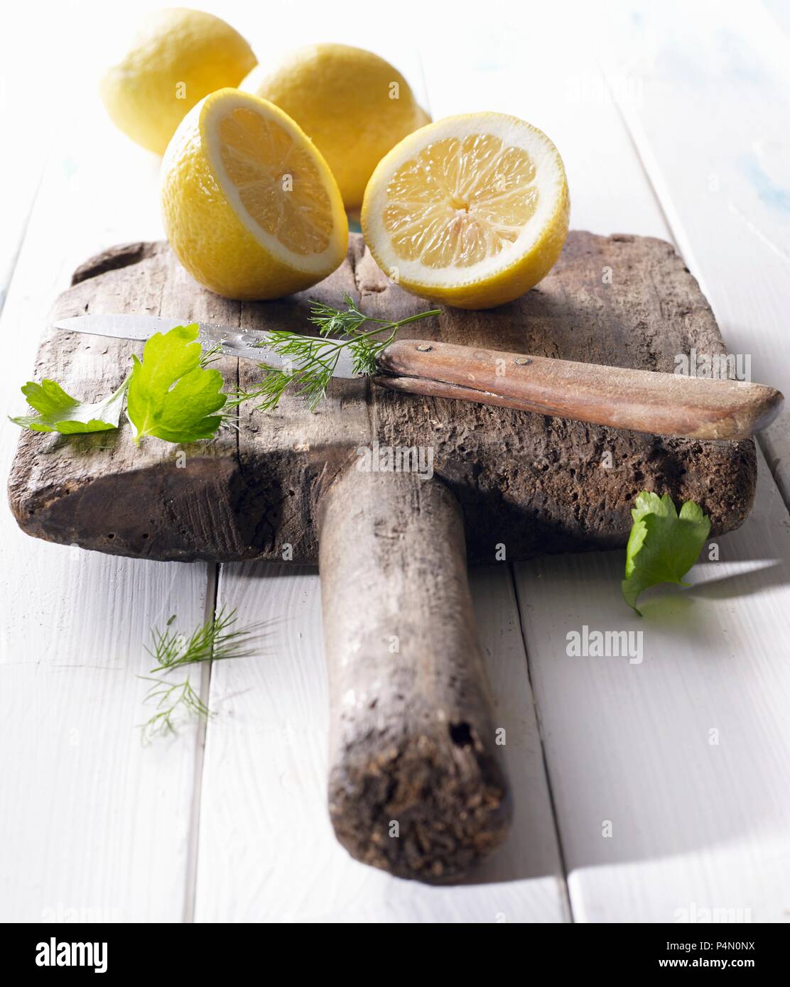 Les citrons coupés en deux sur une vieille planche de bois avec persil, aneth et un couteau Banque D'Images