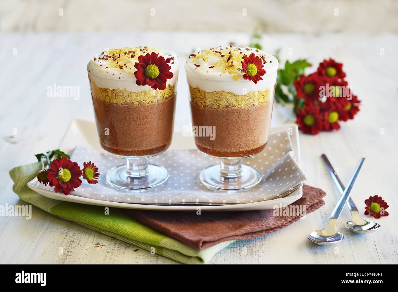 Le chocolat, les céréales et le lait de coco desserts dans deux verres l'un à côté de l'autre et décorées de fleurs fraîches Banque D'Images