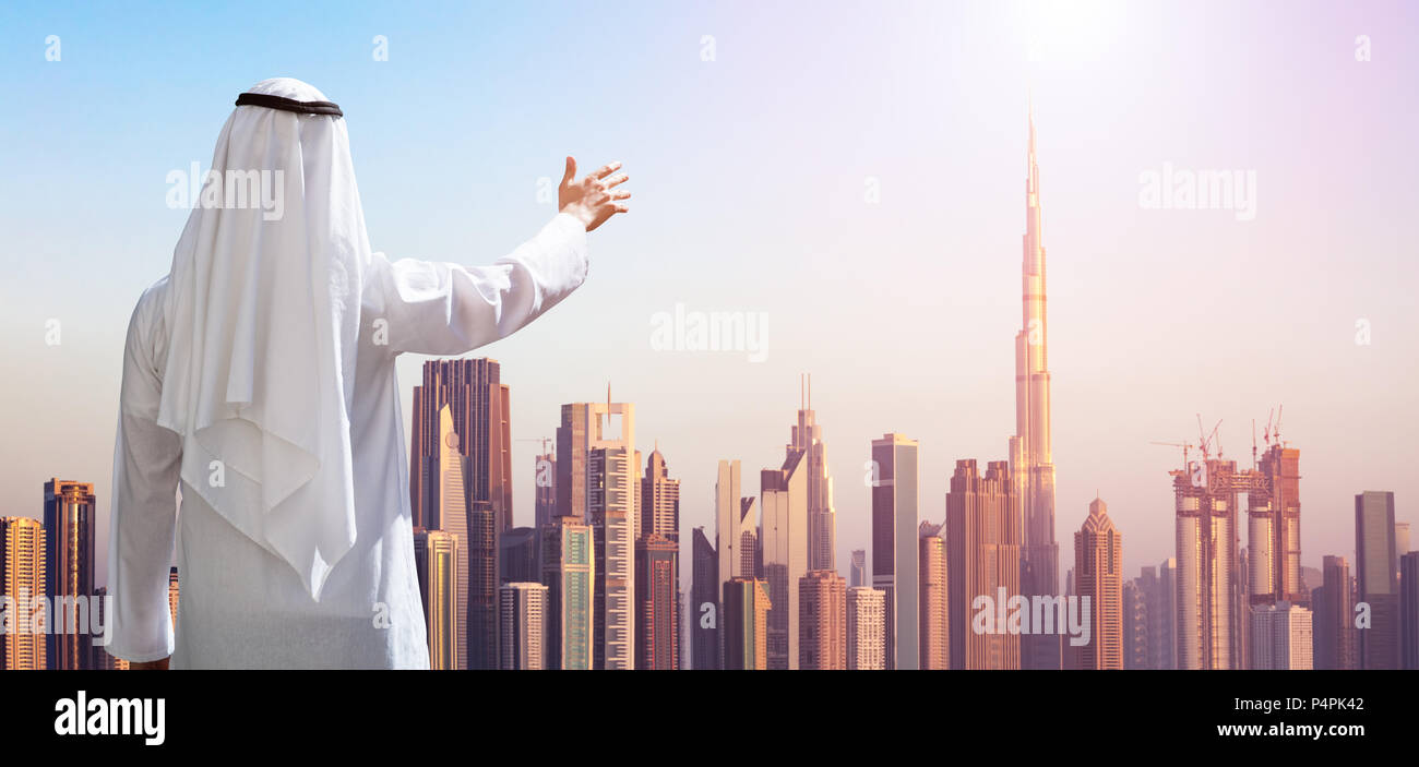 Vue arrière d'un homme arabe Outstretching ses mains à des bâtiments modernes à Dubaï Banque D'Images