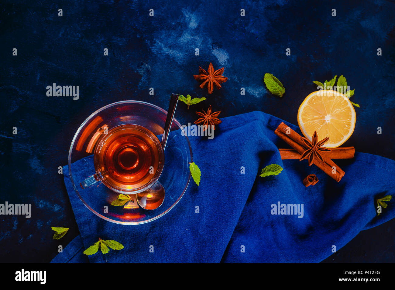 Boisson chaude en-tête avec tasse en verre, , nappes, rondelles de citron, la cannelle, l'anis étoile et de feuilles de menthe sur un fond sombre. Télévision photographie alimentaire sombre Banque D'Images