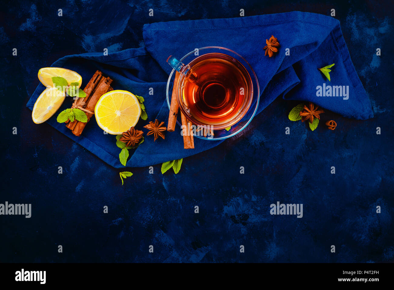 Boisson chaude en-tête avec tasse en verre, , nappes, rondelles de citron, la cannelle, l'anis étoile et de feuilles de menthe sur un fond sombre. Télévision photographie alimentaire sombre Banque D'Images