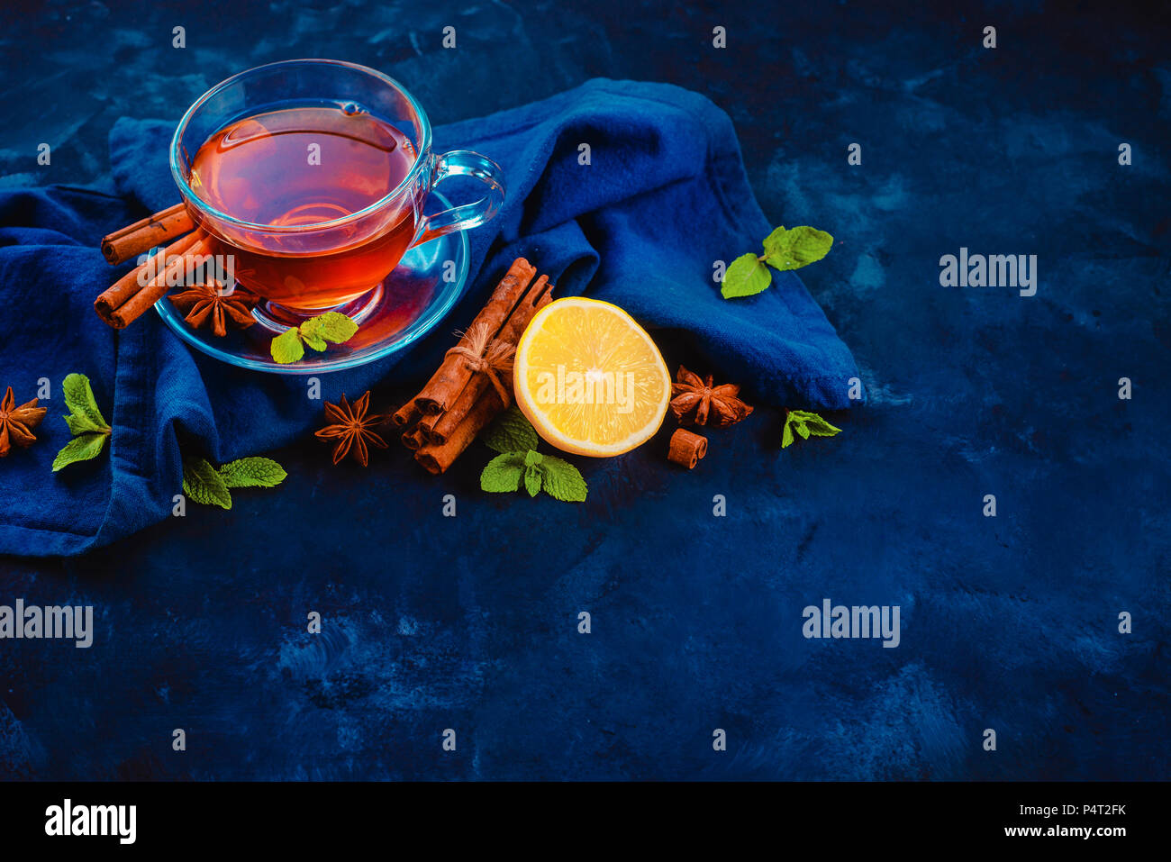 Tasse en verre de thé noir, , nappes, rondelles de citron, la cannelle, l'anis étoile et de feuilles de menthe sur un fond sombre. En-tête de la photographie alimentaire sombre avec l'exemplaire Banque D'Images