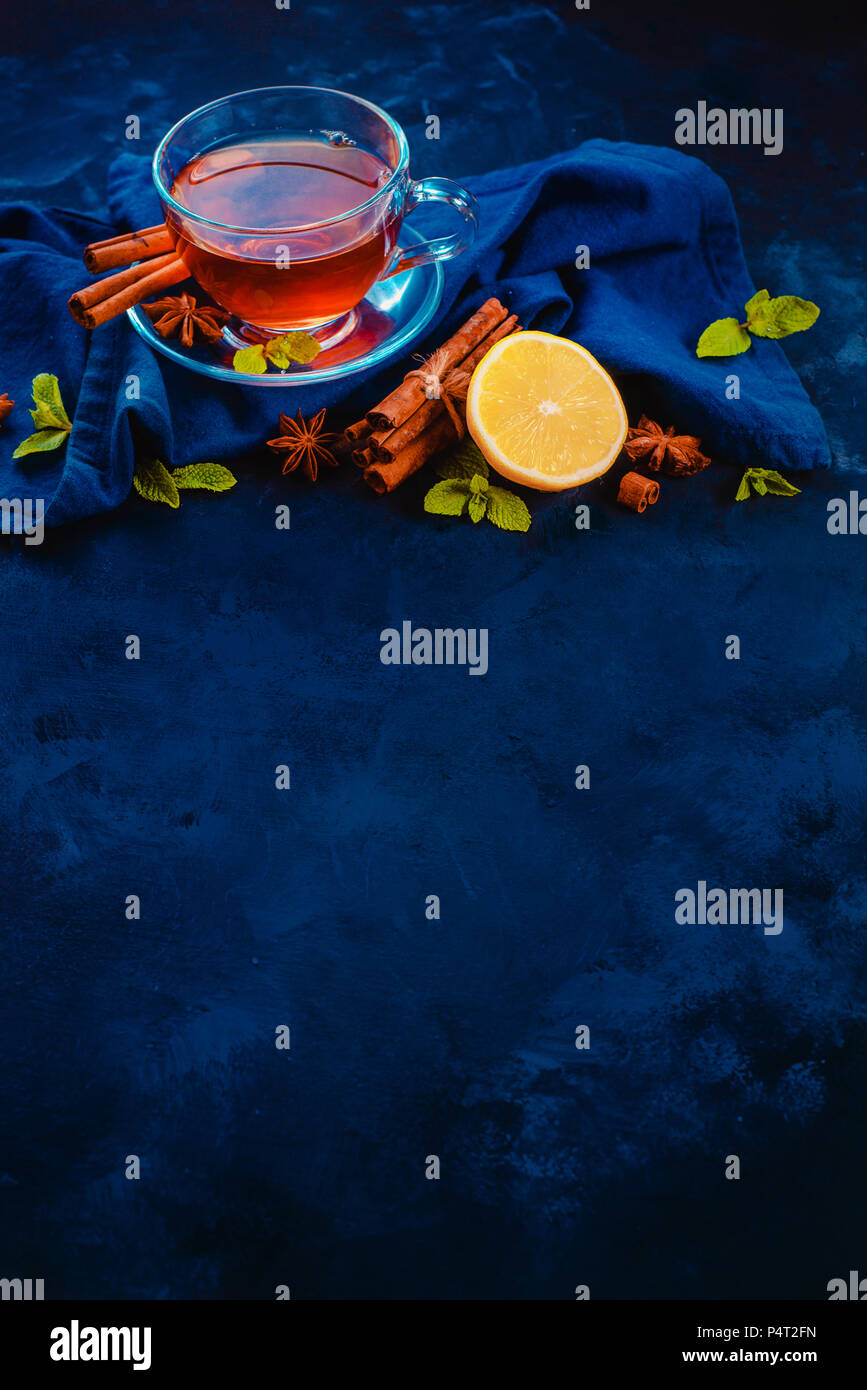 Plateau en verre tasse et soucoupe avec des rondelles de citron, la cannelle, l'anis étoile et de feuilles de menthe sur un fond sombre avec des draps serviette. Des couleurs vibrantes boisson chaude fla Banque D'Images