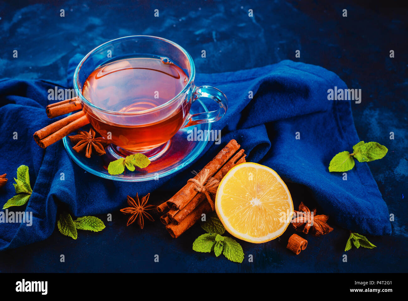 Plateau en verre tasse et soucoupe avec des rondelles de citron, la cannelle, l'anis étoile et de feuilles de menthe sur un fond sombre avec des draps serviette. Des couleurs vibrantes boisson chaude fla Banque D'Images