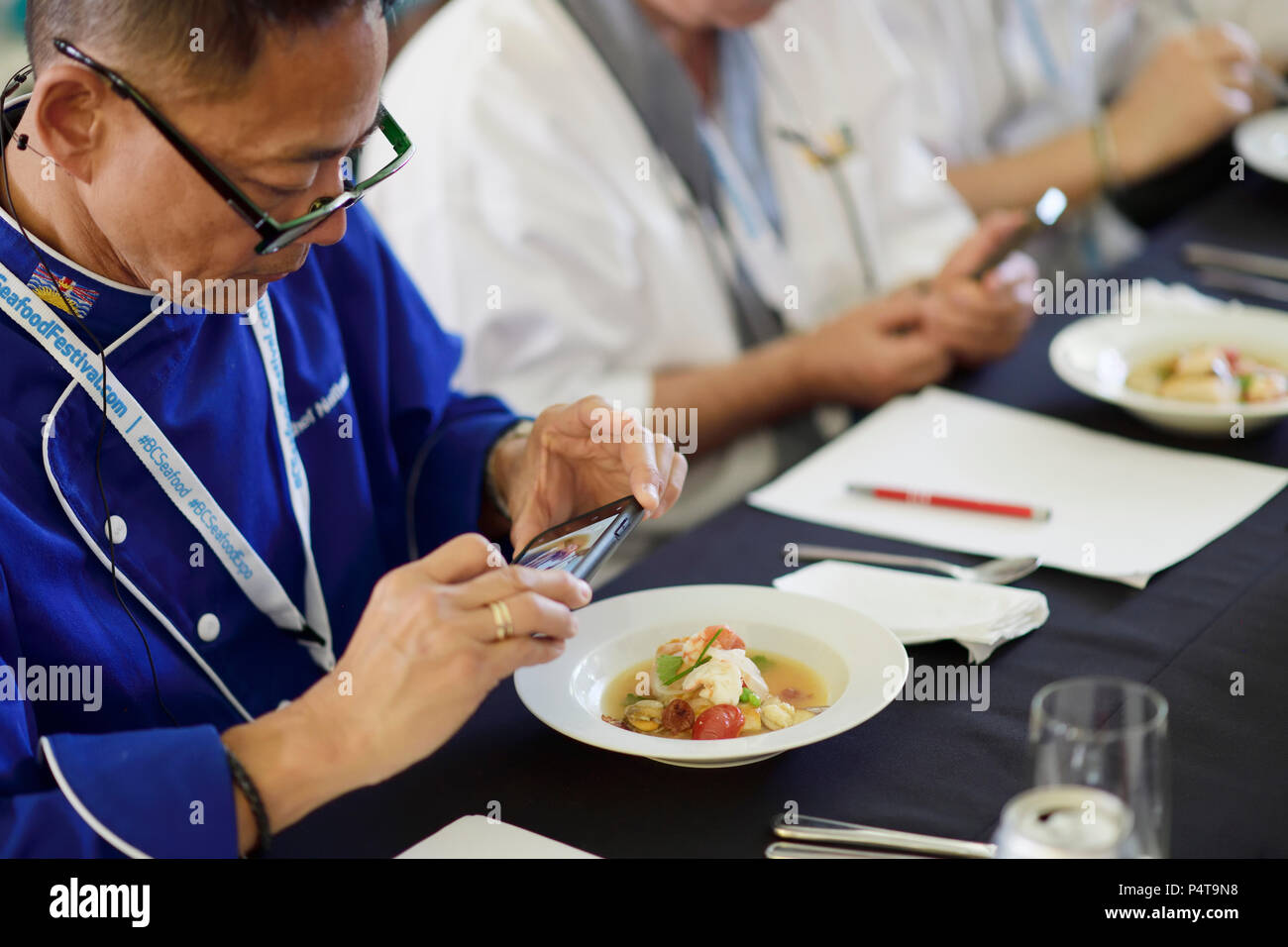 La concurrence du chef juge, Chef Nathan Fong, faire des photos d'un repas gastronomique au Festival des fruits de mer de la C.-B. 2018 Défi Chef dans la vallée de la Comox, en colonne Banque D'Images