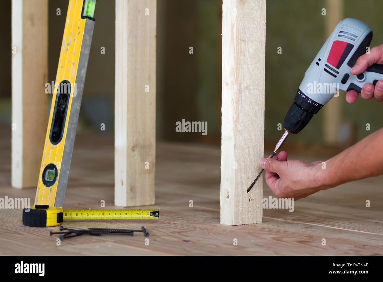 Close-up des mains du travailleur à l'aide d'un tournevis sur le contexte d'outils professionnels et cadres en bois pour les murs de chambre mansardée inachevé sous recons Banque D'Images