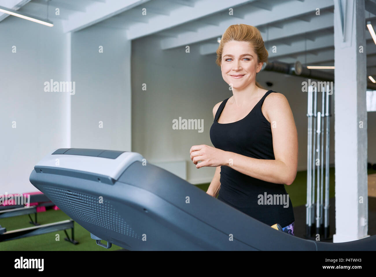 Portrait of smiling woman sur tapis roulant à la salle de sport Banque D'Images