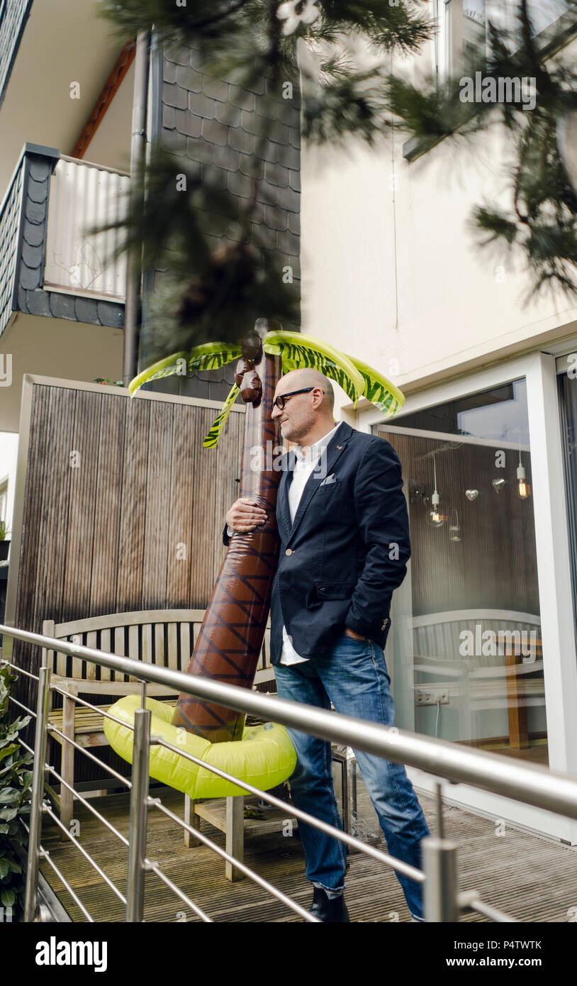 Senior businessman debout dans son jardin, tenant une palme en caoutchouc, rêvant de vacances Banque D'Images